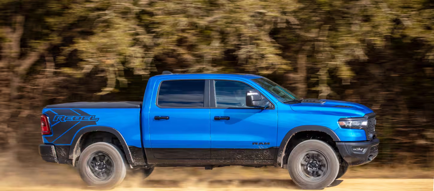 A blue 2025 RAM 1500 driving through woods